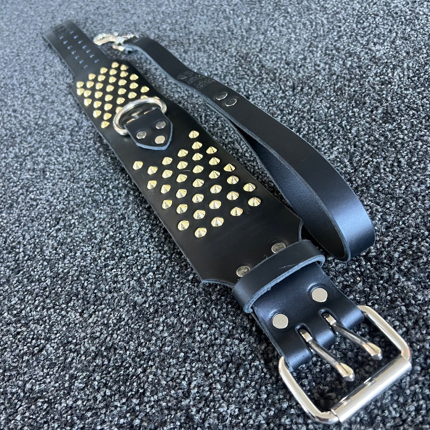 Black leather strap with gold studs and silver buckles on a textured gray background