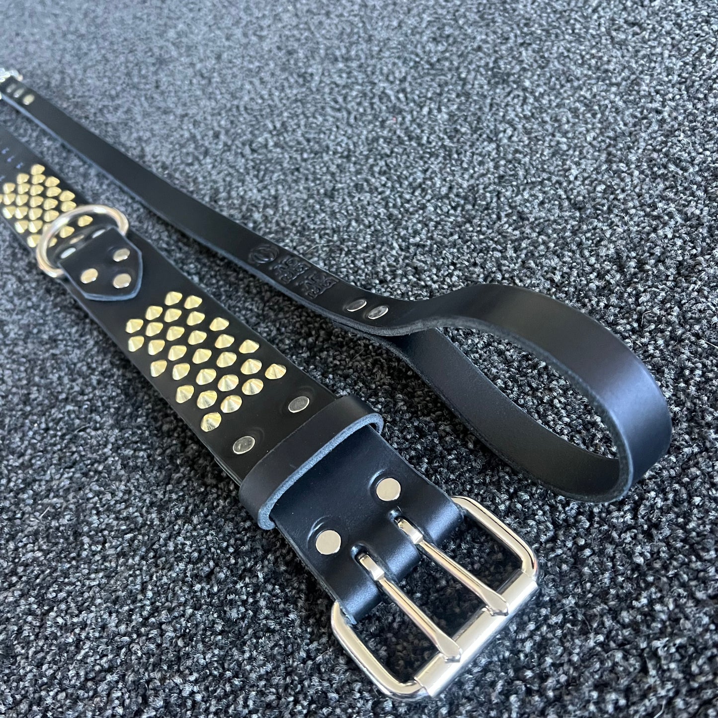 Black leather belt with gold studs and silver buckle on a textured gray background