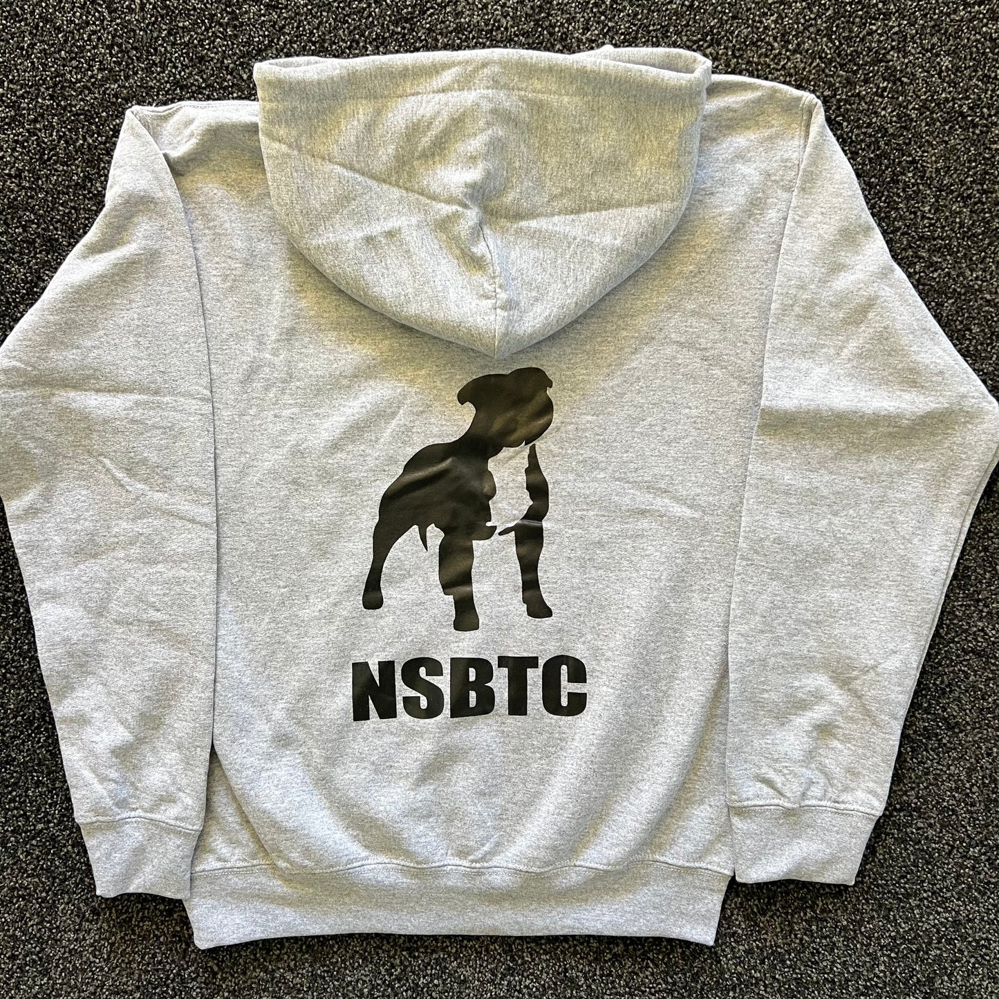 Gray hoodie with a black silhouette of a dog and 'NSBTC' text on the back, laid flat on a dark surface.