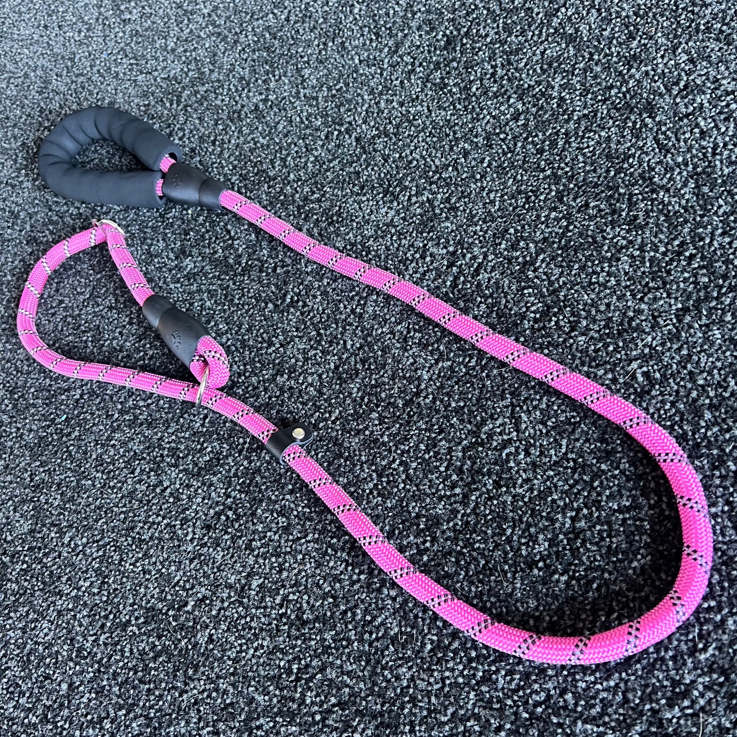 Pink dog leash with black handle on a textured gray surface