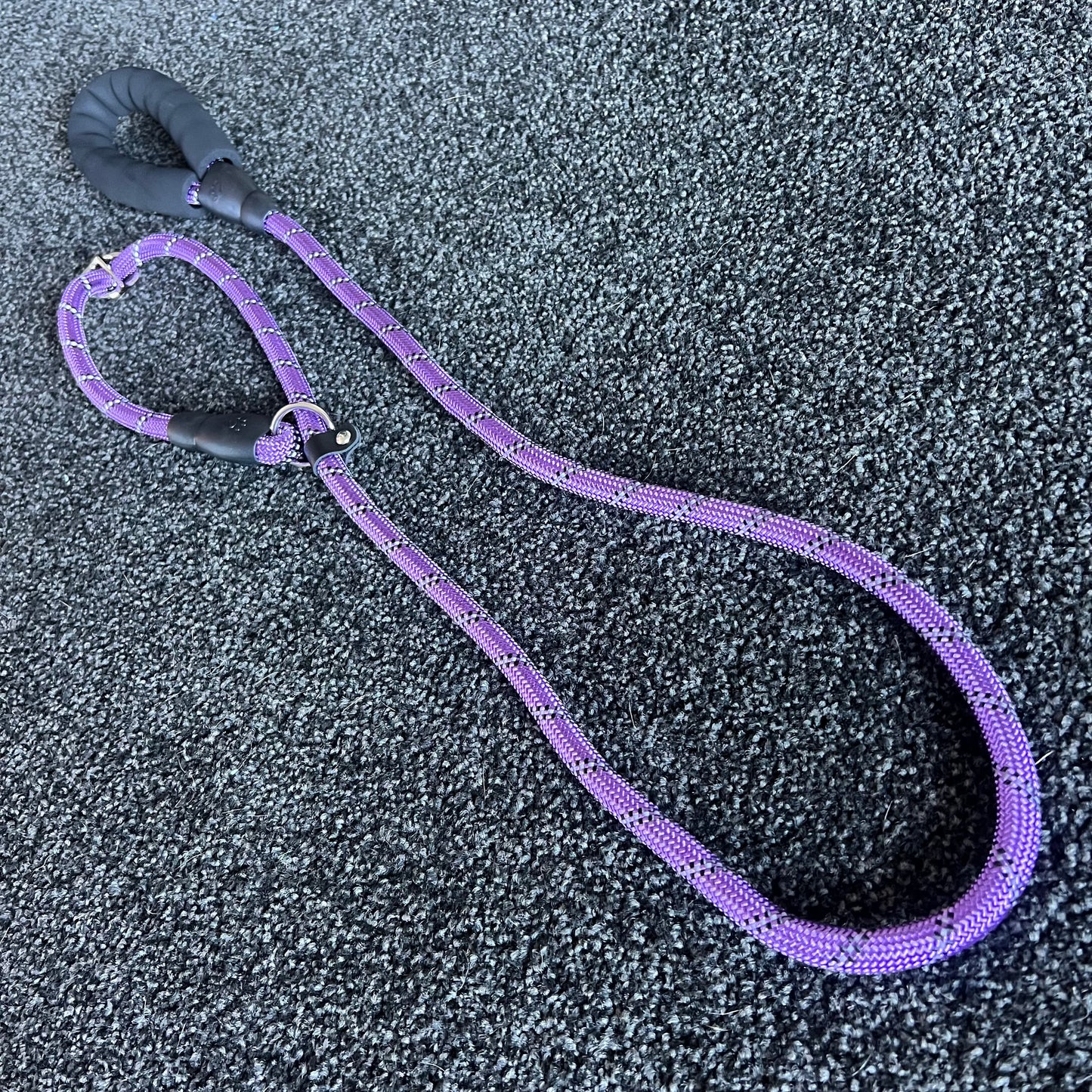 Purple dog leash with black handle on a textured gray surface