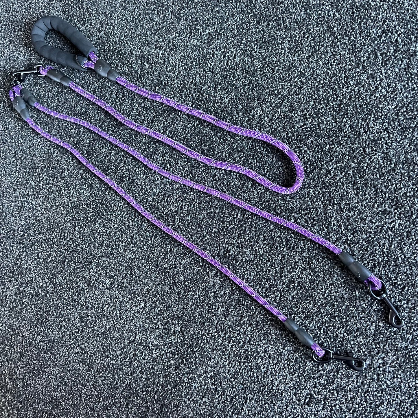 Purple dog leash with black handles on a textured gray surface