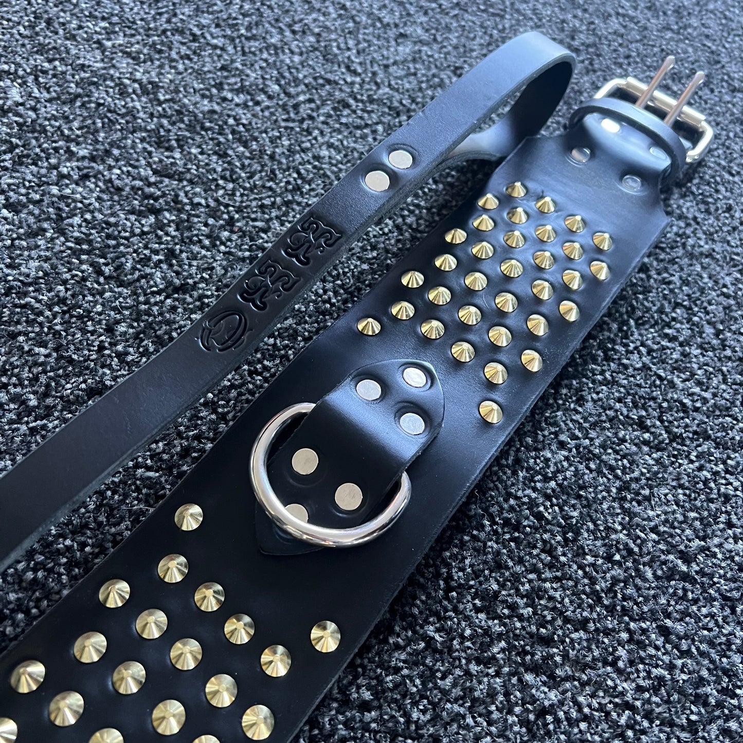 Black leather strap with gold studs on a textured black background
