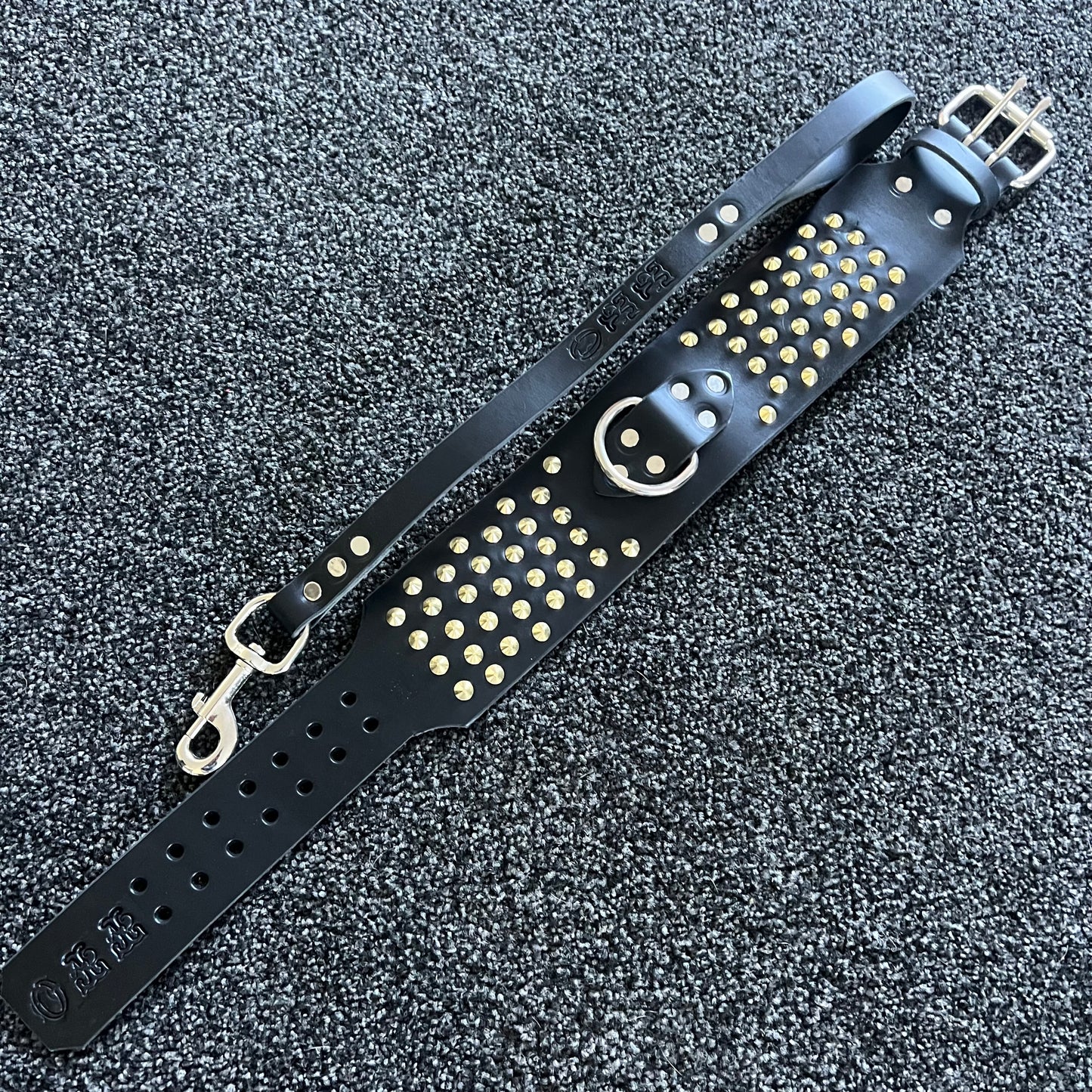 Black leather strap with gold studs and a smiley face design on a textured black background