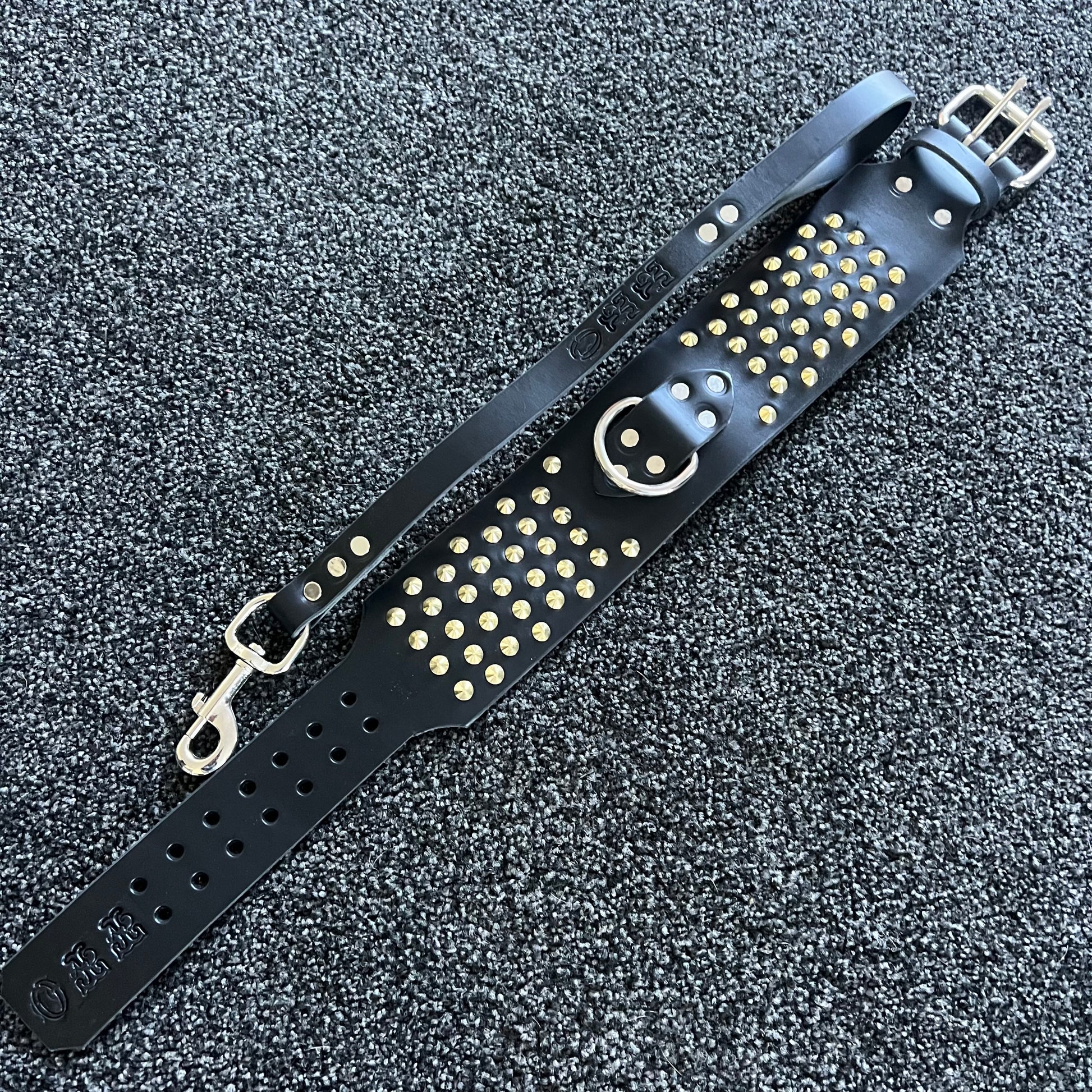 Black leather strap with gold studs and a smiley face design on a textured black background