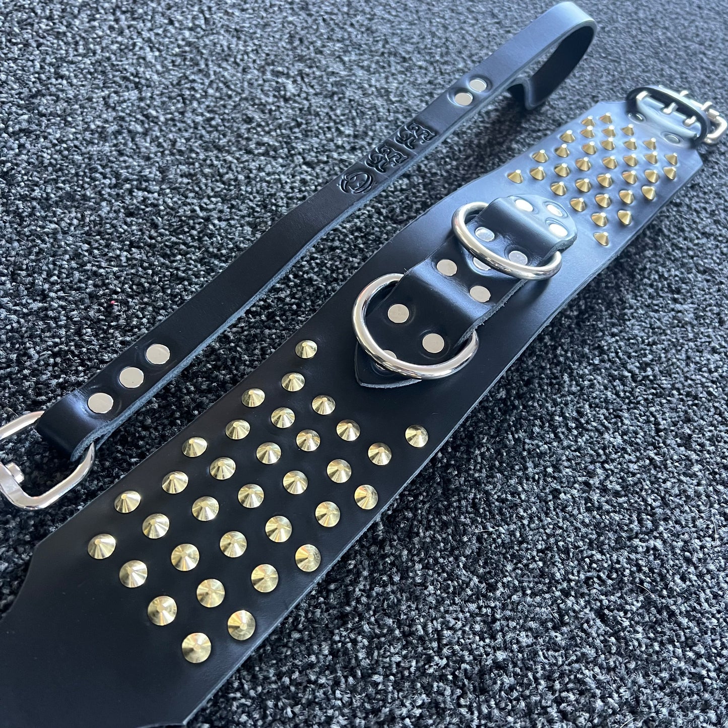 Black leather strap with gold studs on a textured black surface