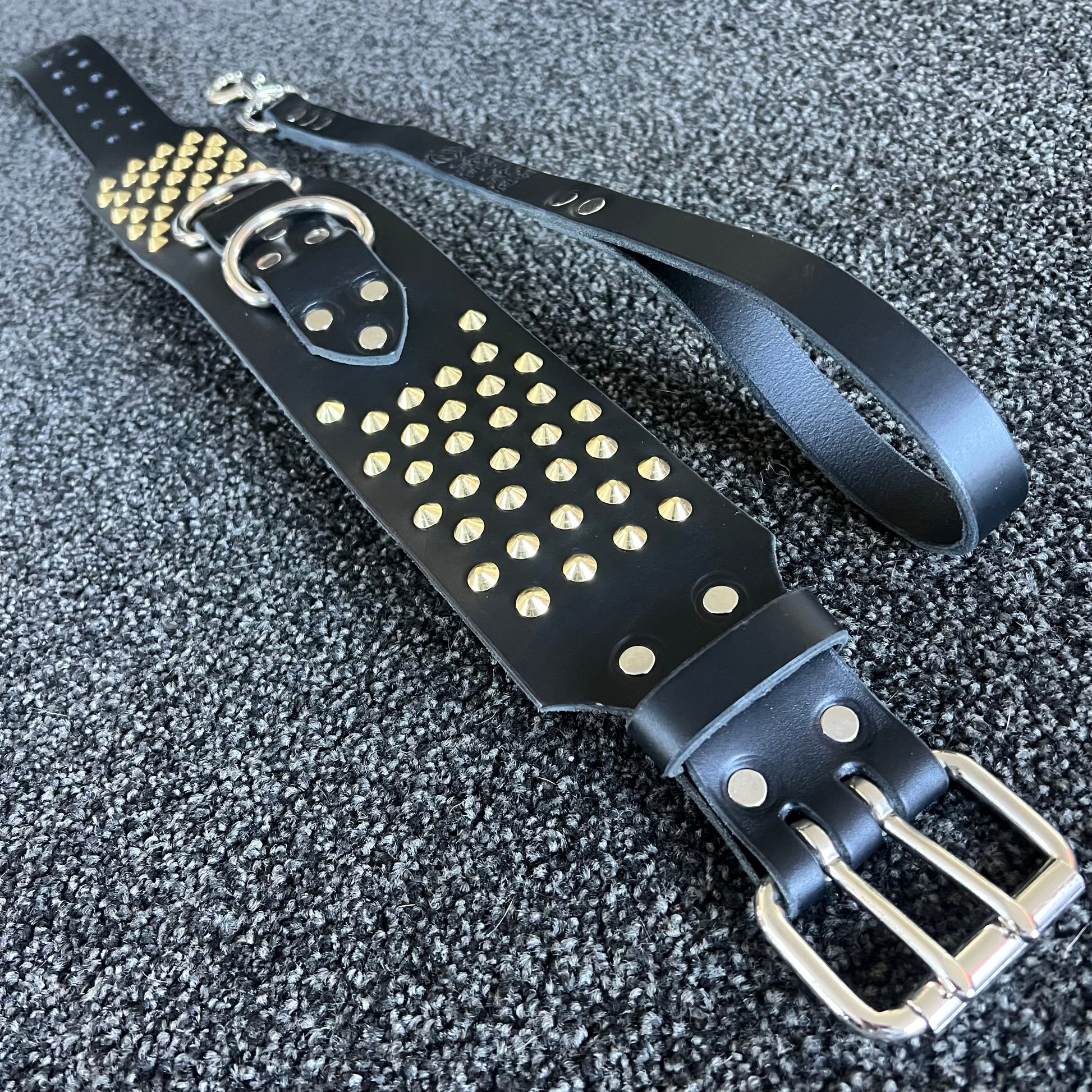 Black leather belt with gold studs and silver buckle on a textured black background