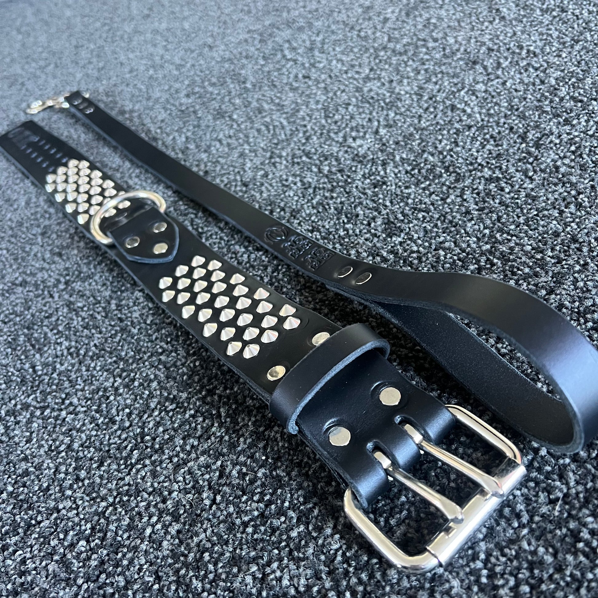 Black leather belt with silver studs and buckle on a textured gray surface
