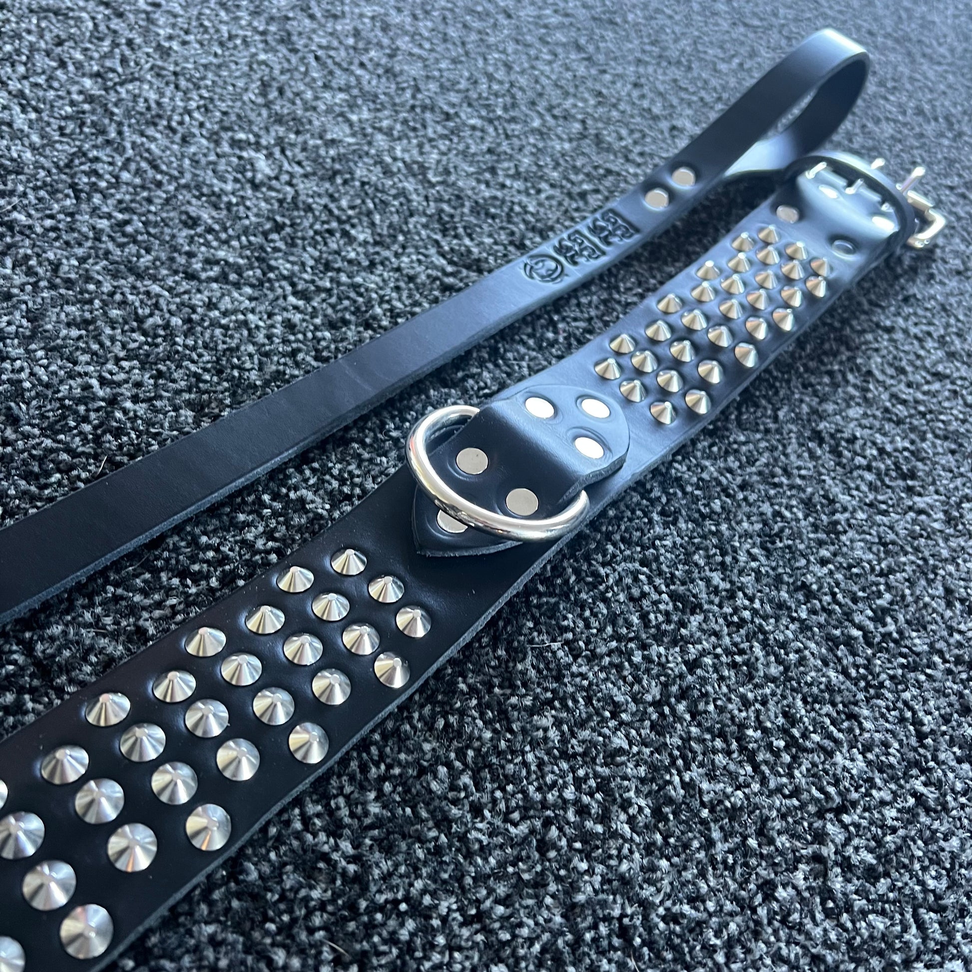 Black leather belt with silver studs and a metal ring on a textured black surface