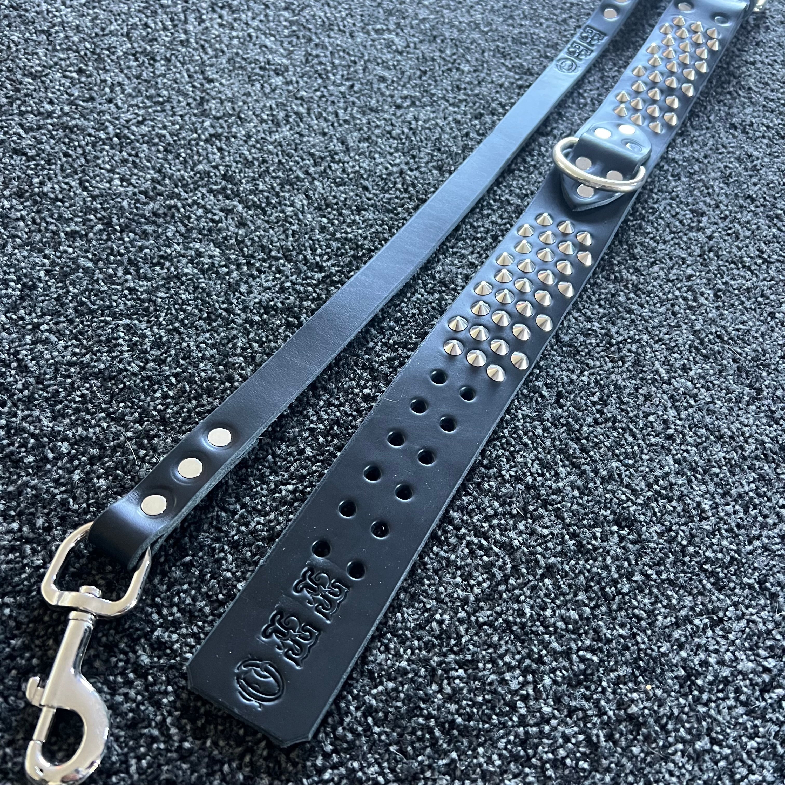 Black leather dog collar with studs and a metal clasp on a textured black surface