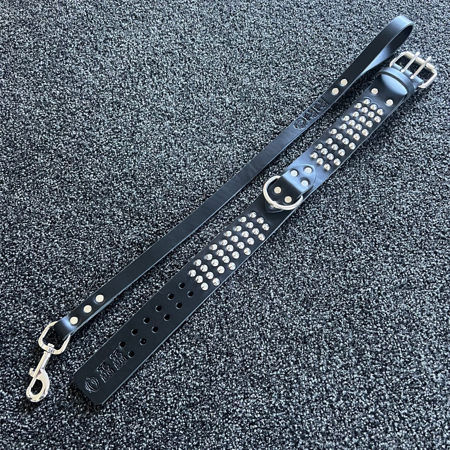 Black leather strap with silver studs and hardware on a textured gray surface