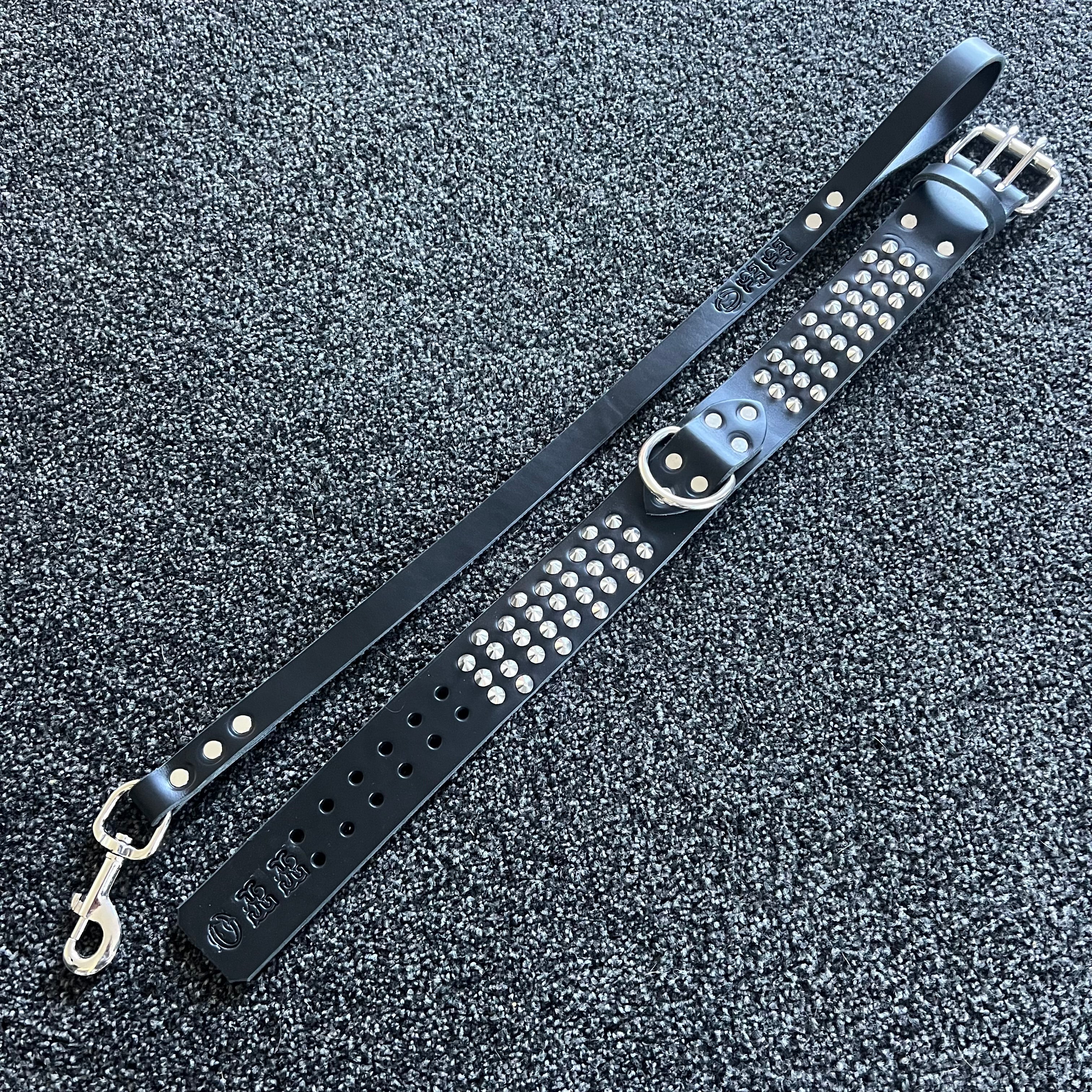 Black leather strap with silver studs and hardware on a textured gray surface