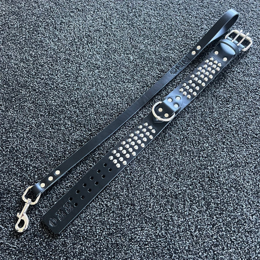 Black leather strap with silver studs and hardware on a textured gray surface
