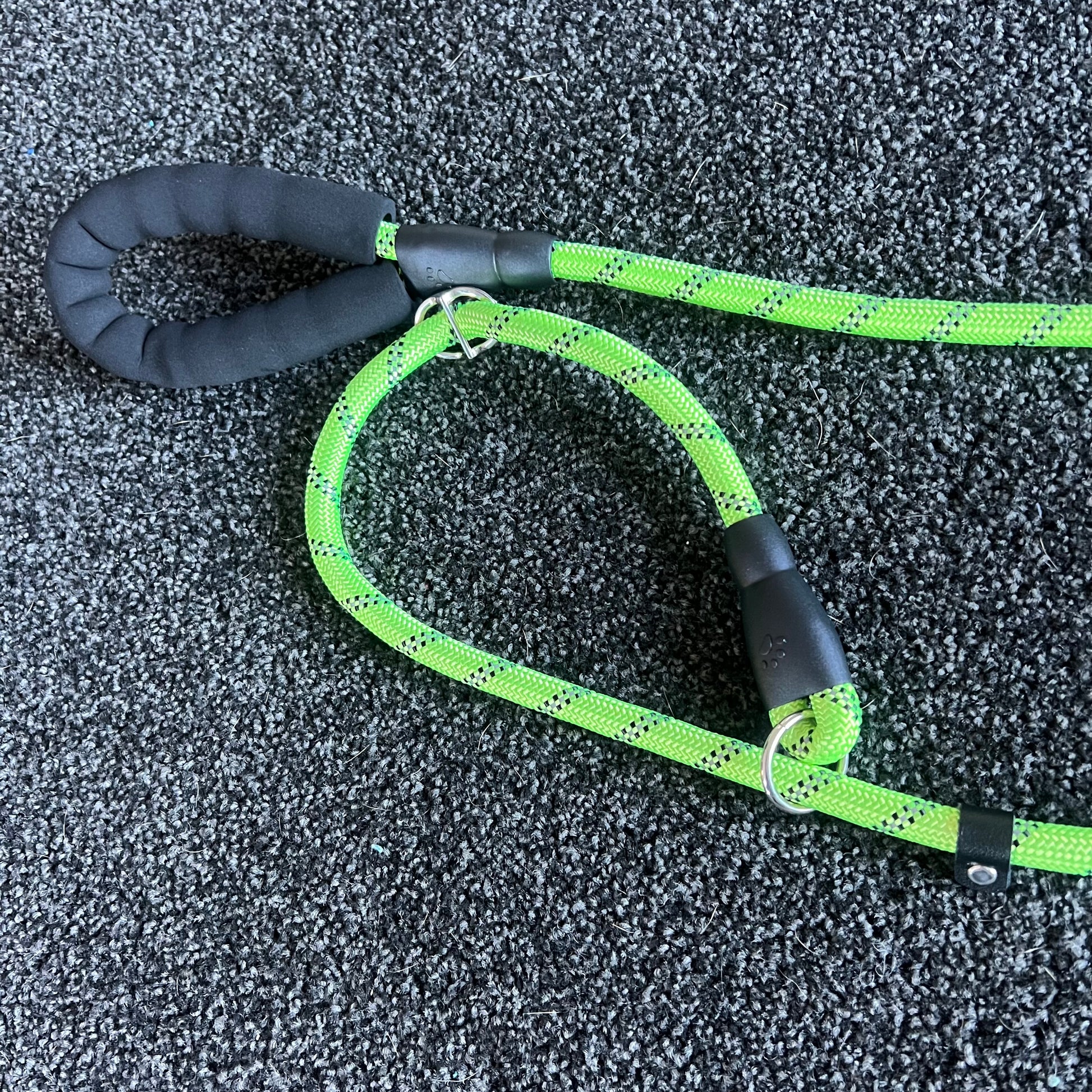 Green dog leash with black handle on a textured gray surface