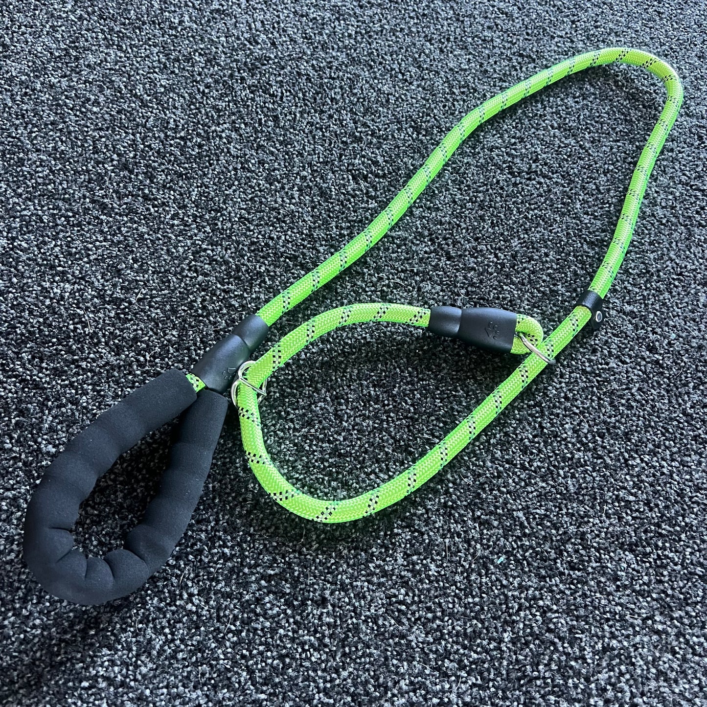 Green dog leash with black handle on a textured surface