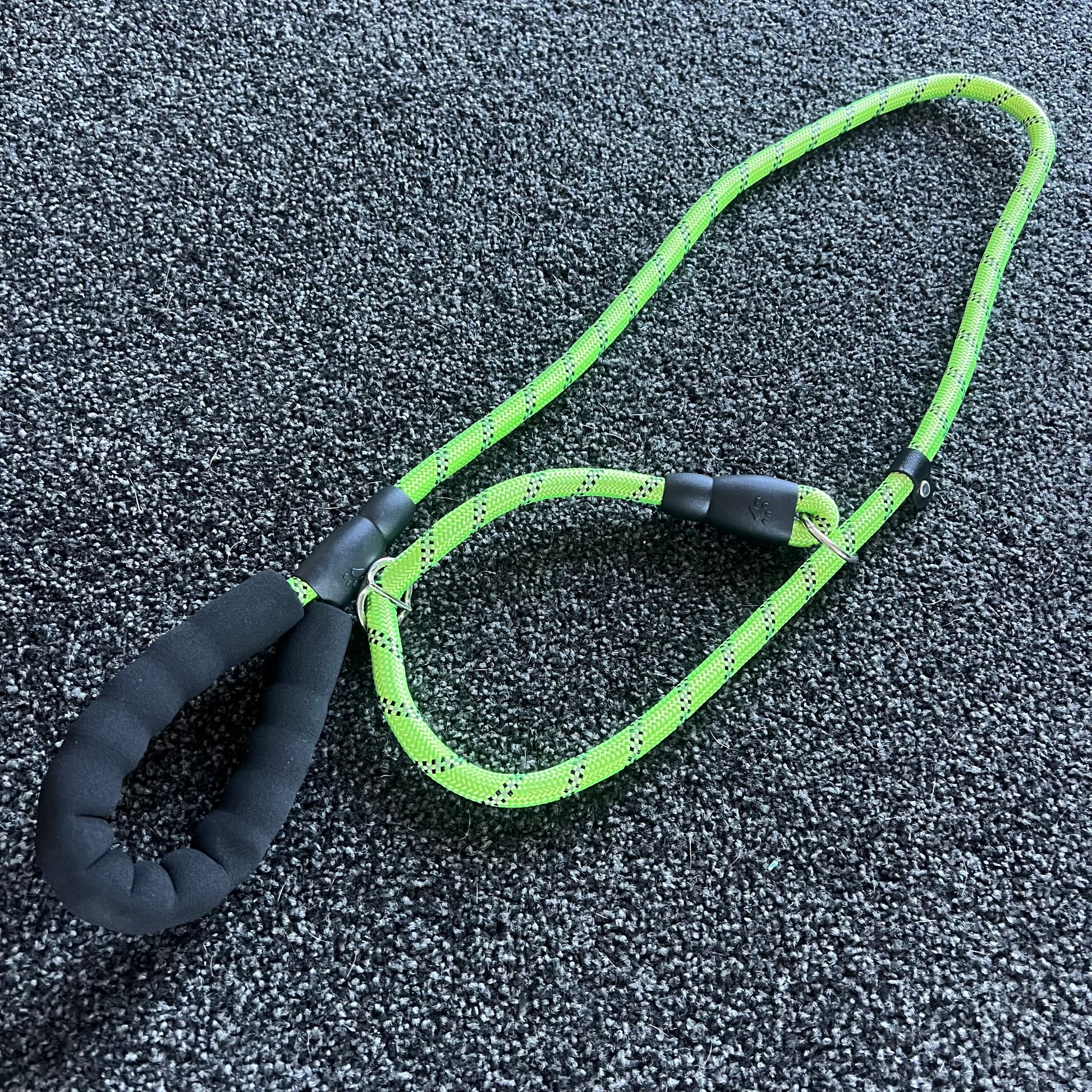 Green dog leash with black handle on a textured surface