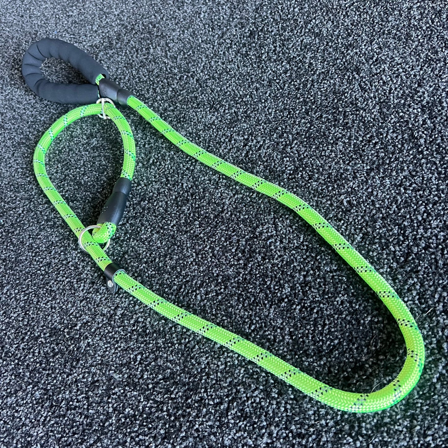 Green dog leash with black handle on a textured gray surface