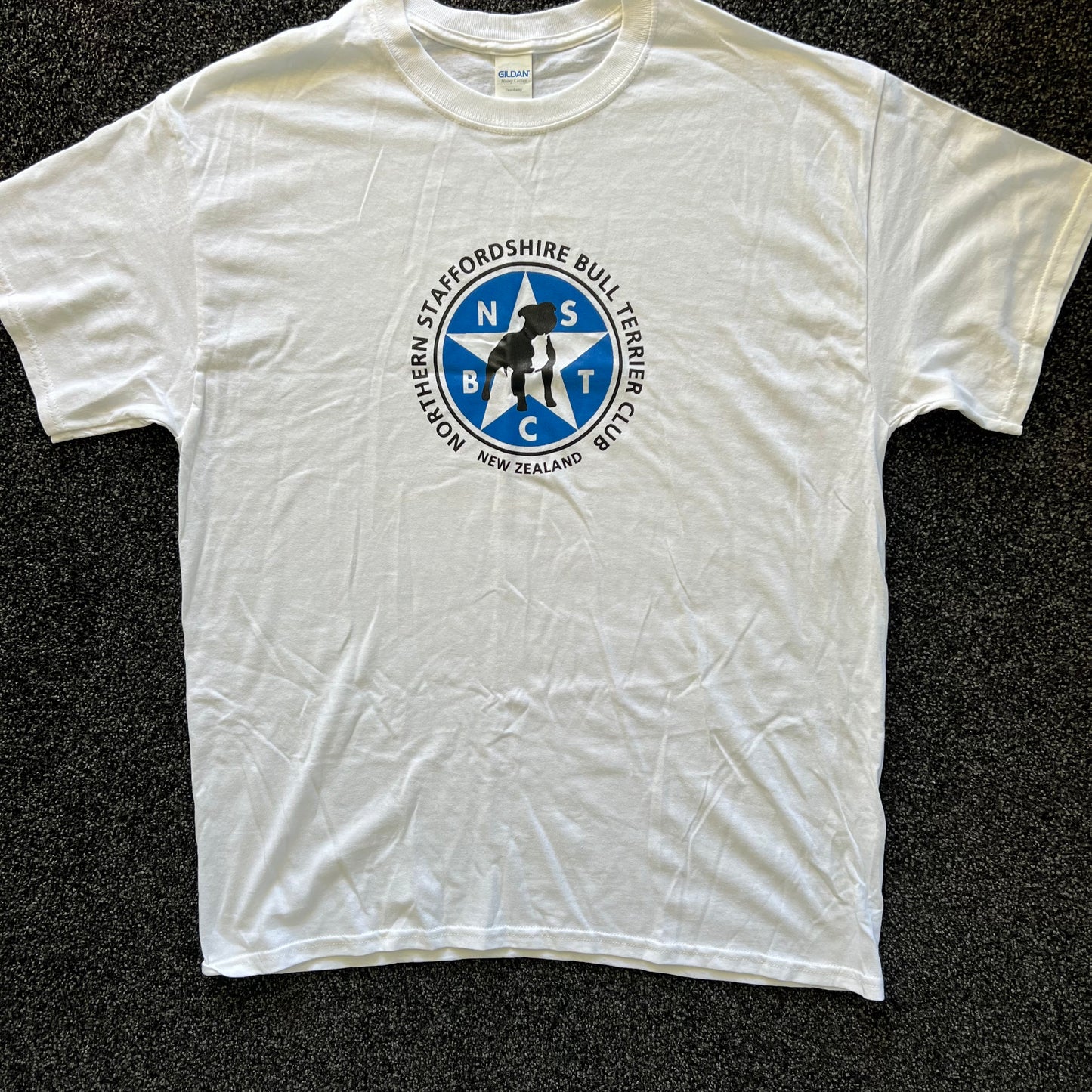 White t-shirt with a blue and black logo on a dark textured background