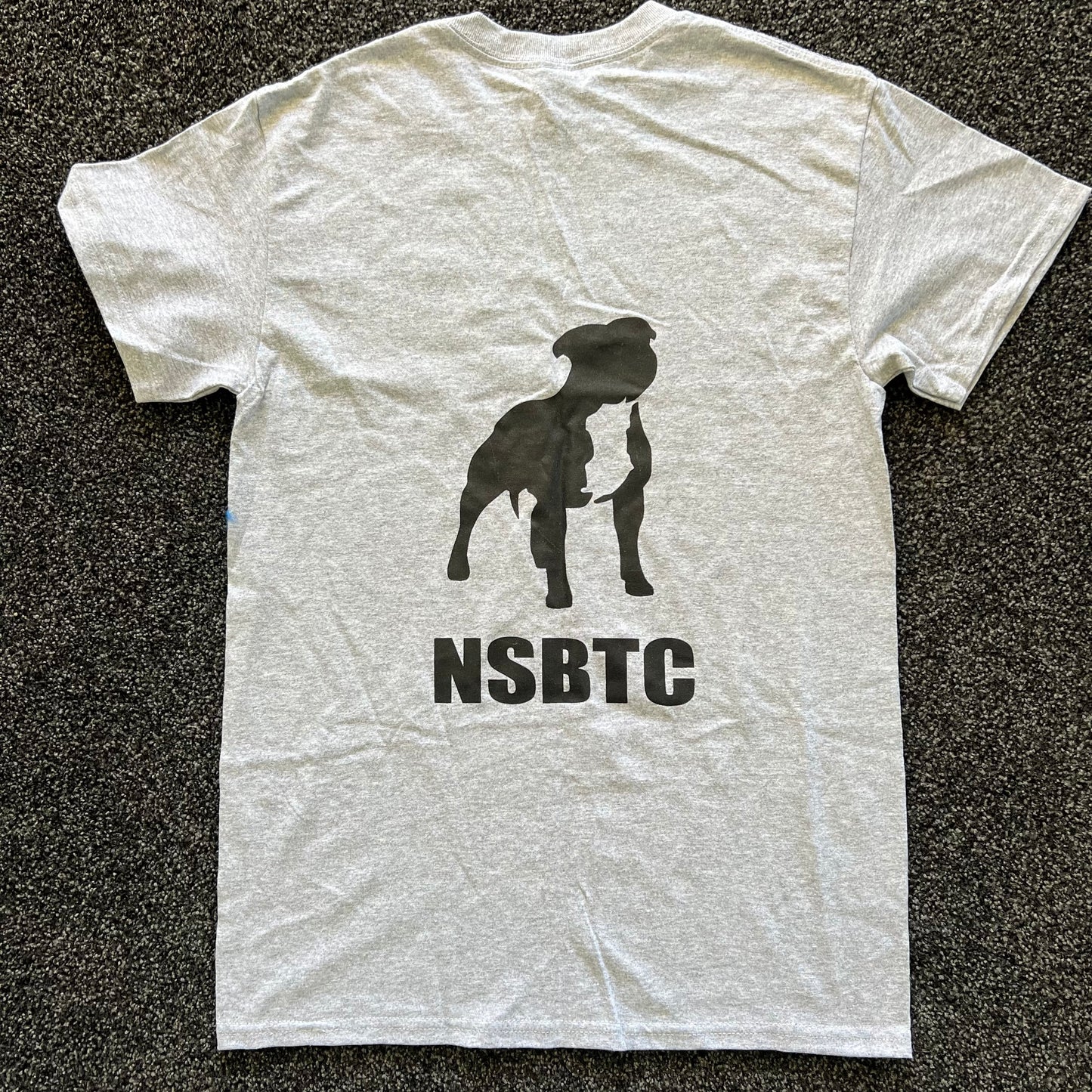 White t-shirt with black dog silhouette and 'NSBTC' text on a dark textured background