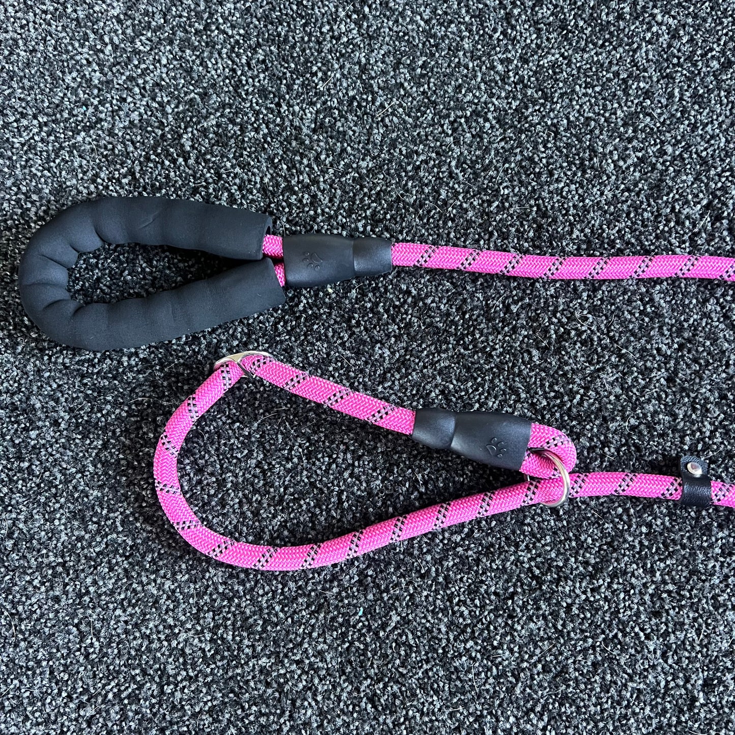 Pink dog leash with black handle on a textured gray surface