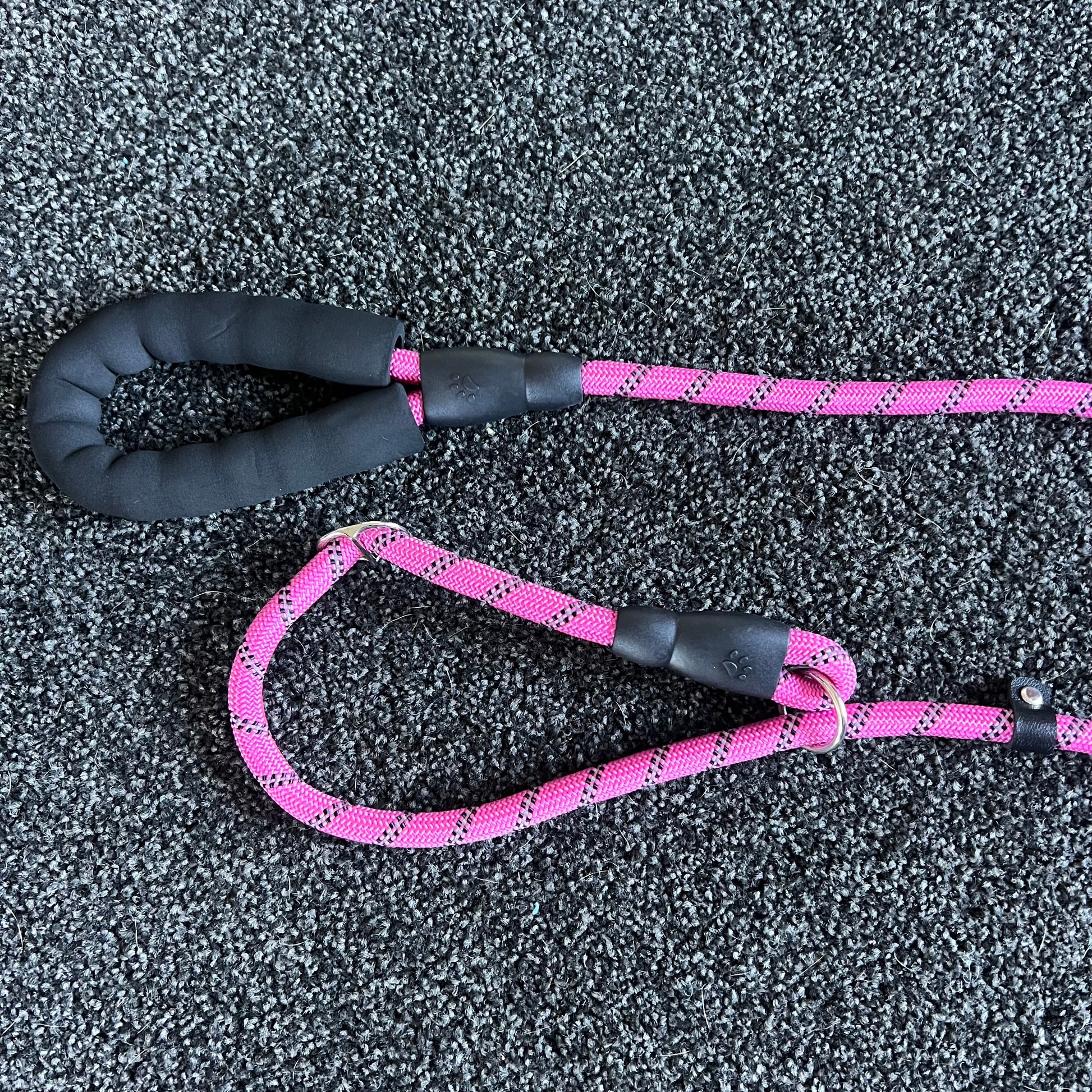 Pink dog leash with black handle on a textured gray surface
