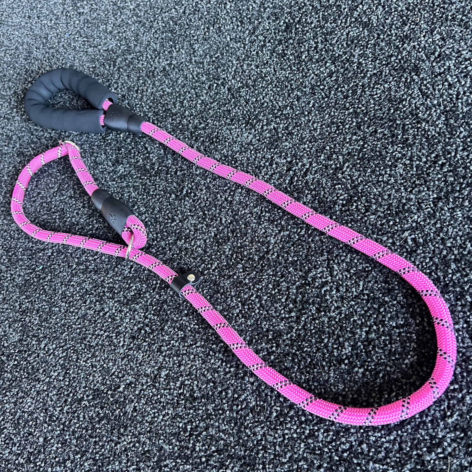 Pink dog leash with black handle on a textured gray surface