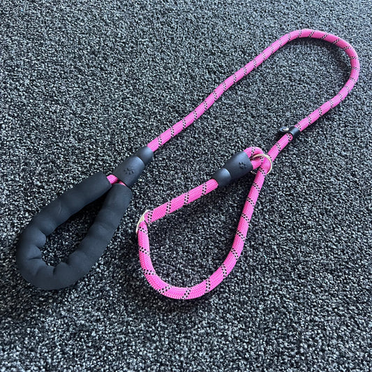 Pink dog leash with black handle on a textured gray surface