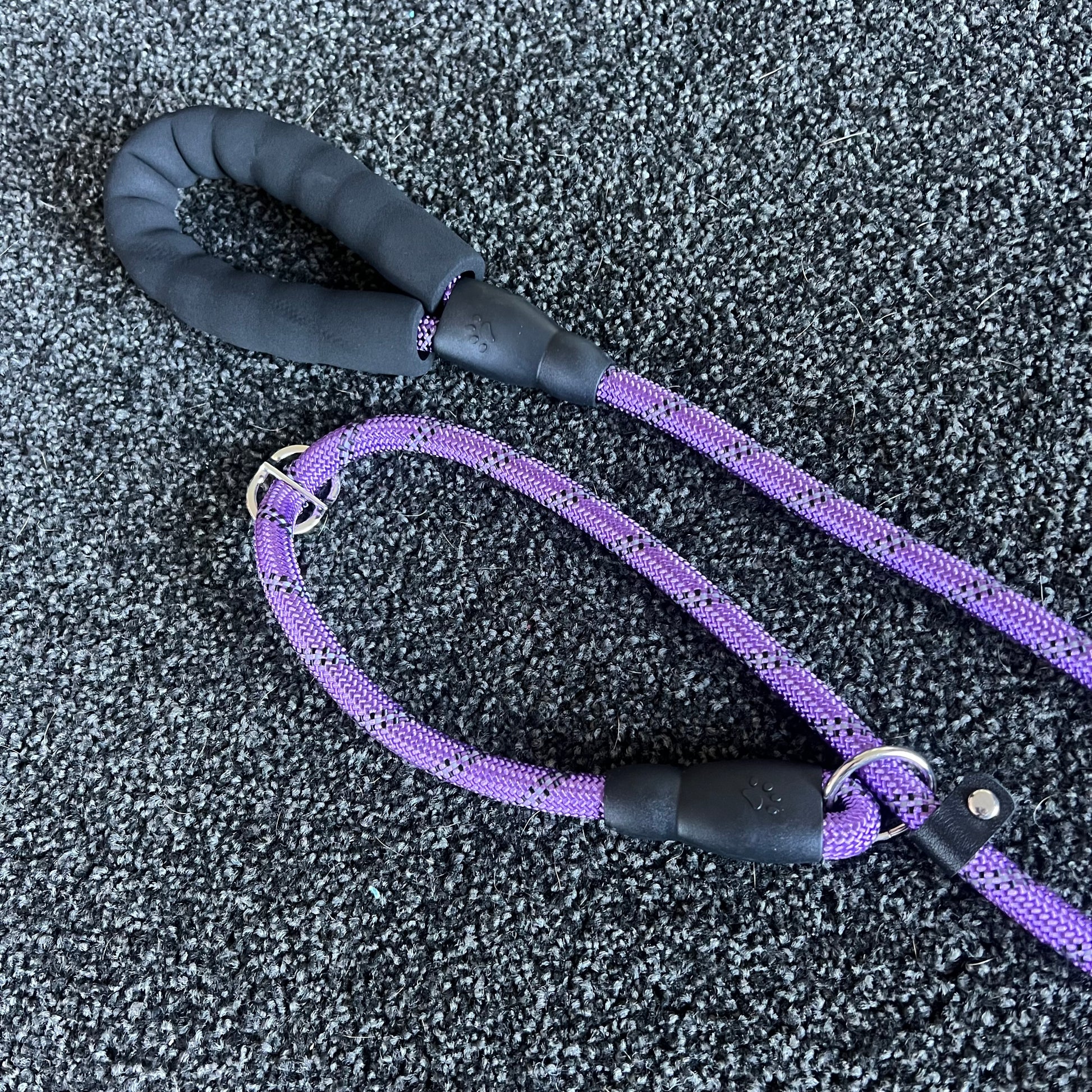Purple dog leash with black handle on a textured gray surface