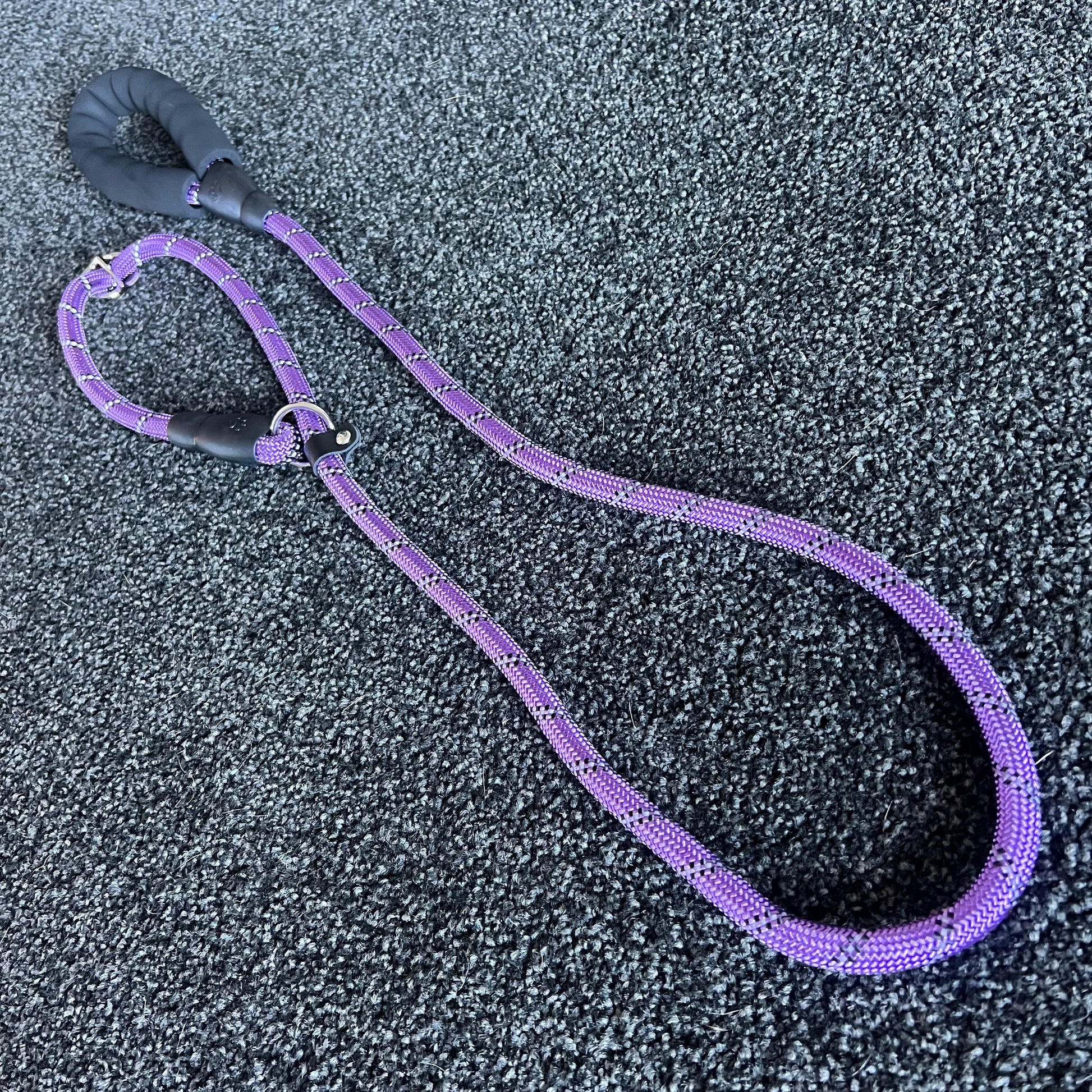Purple dog leash with black handle on a textured gray surface
