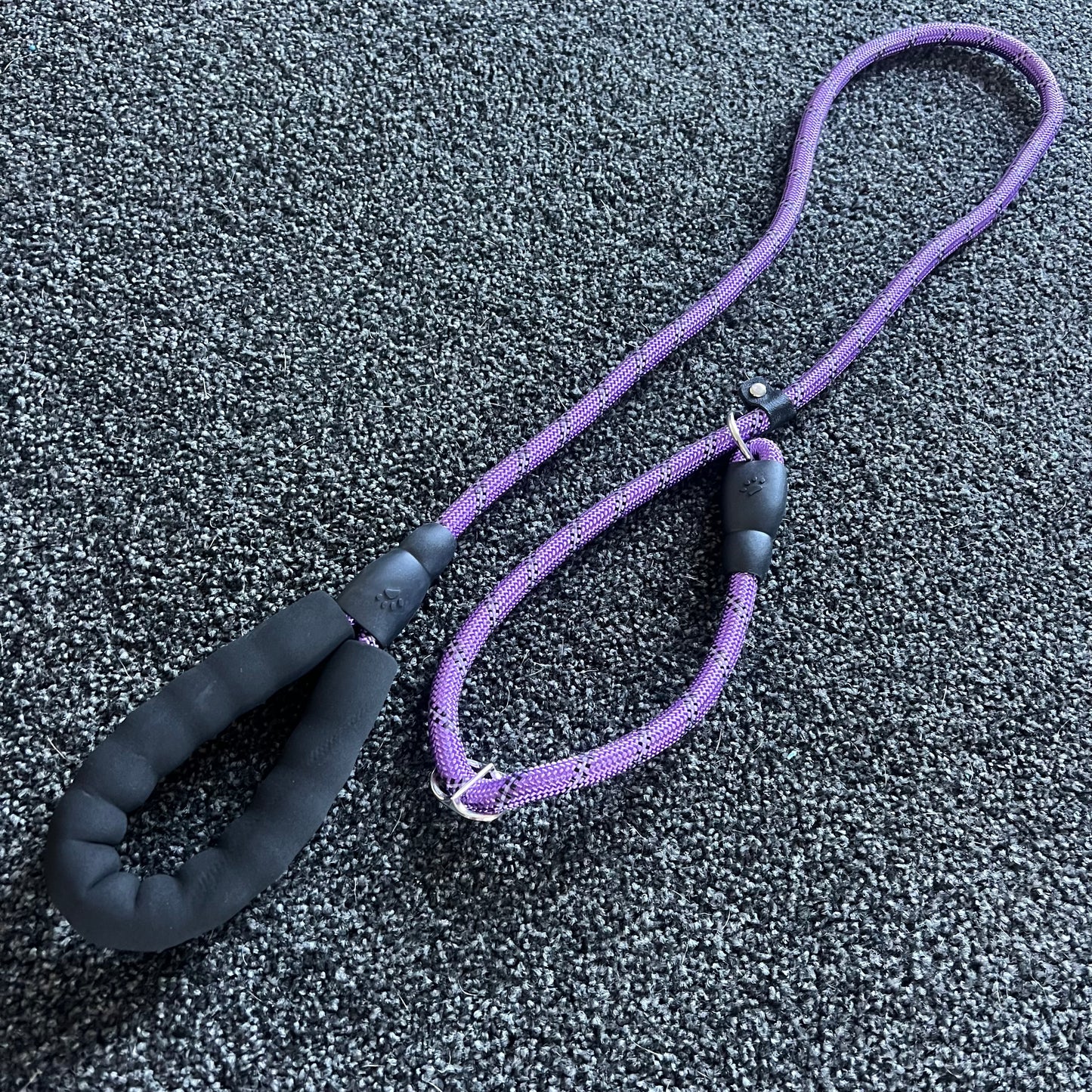 Purple dog leash with black handle on a textured gray surface