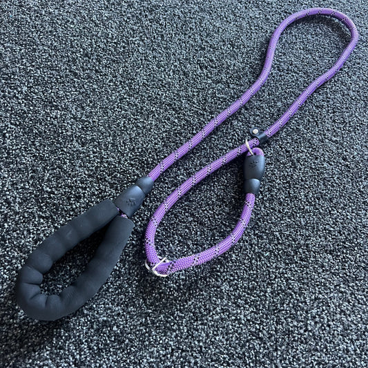 Purple dog leash with black handle on a textured gray surface