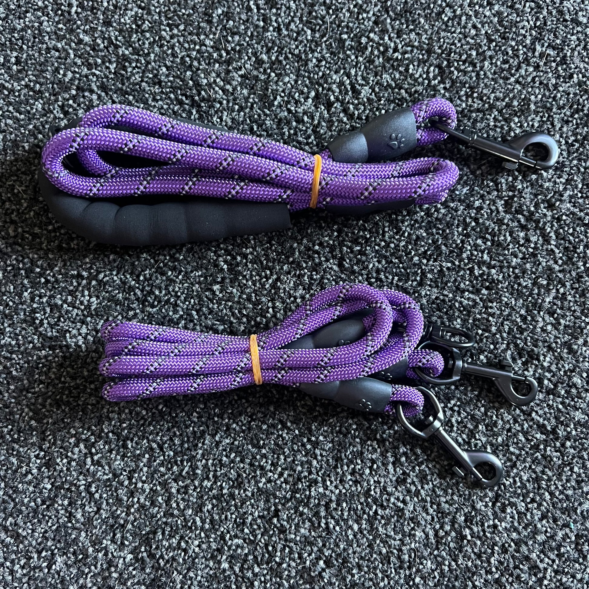 Two purple dog leashes with black handles on a gray textured surface