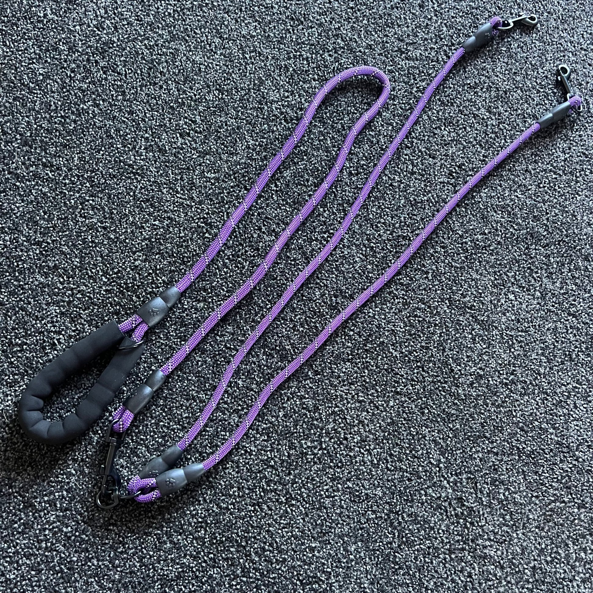 Purple dog leash with black handles on a dark textured surface