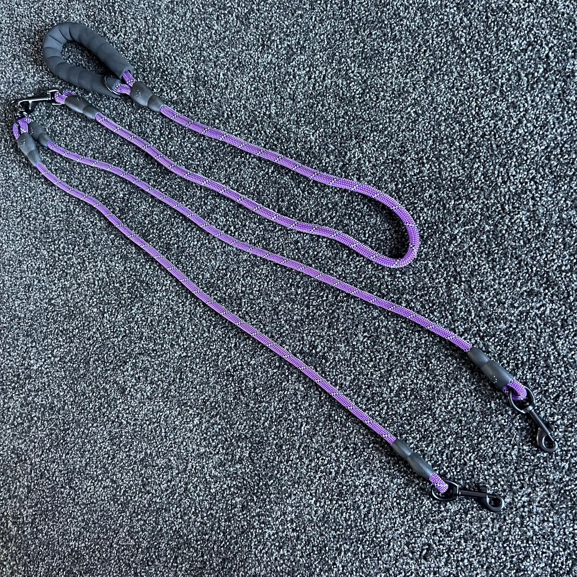Purple dog leash with black handles on a textured gray surface