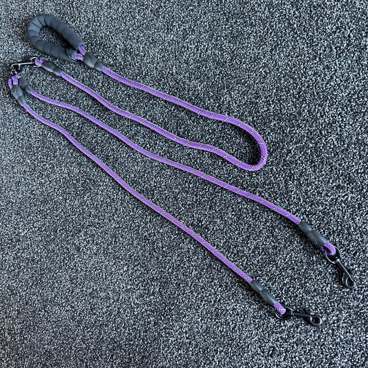 Purple dog leash with black handles on a textured gray surface