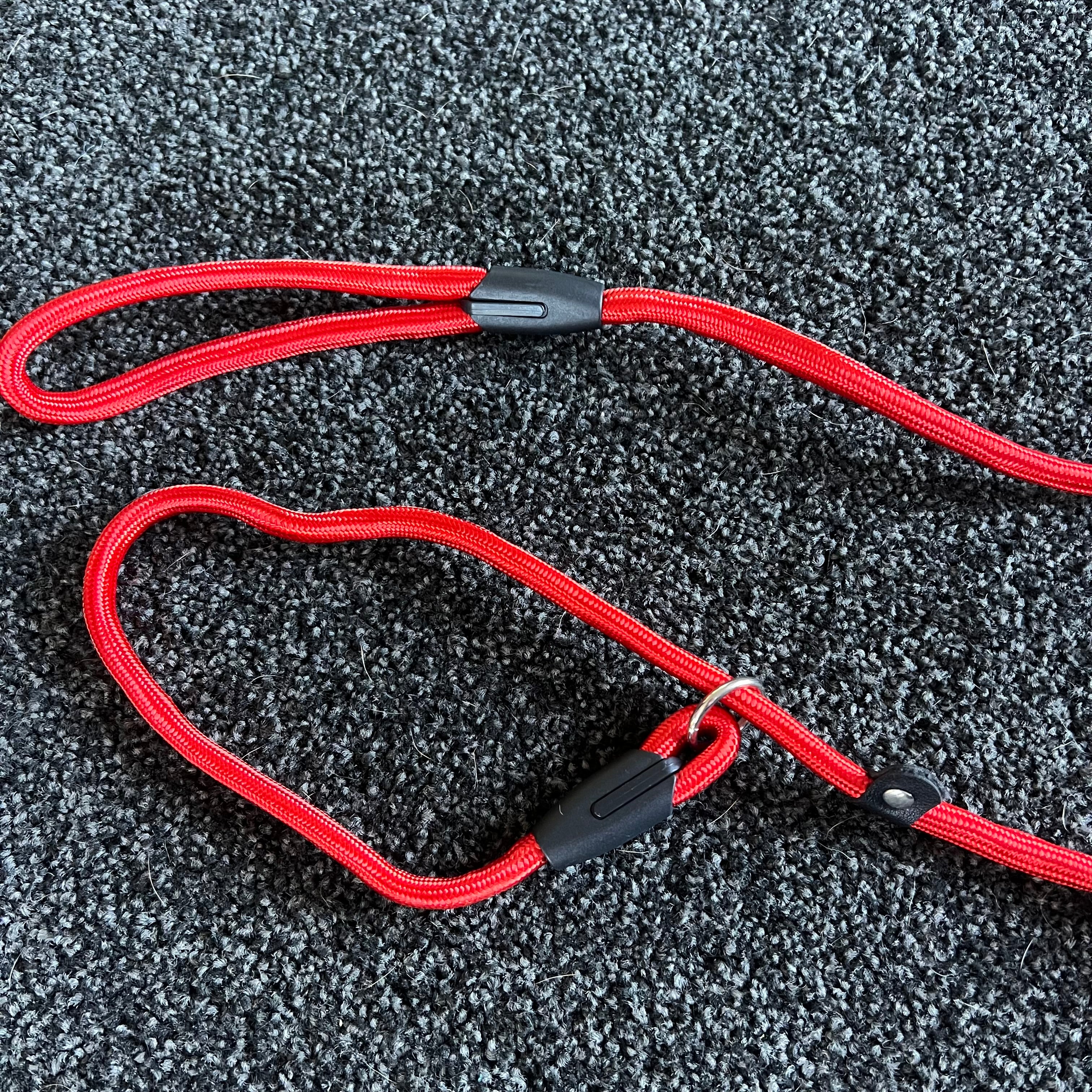 Red dog leash with black plastic clips on a textured gray surface