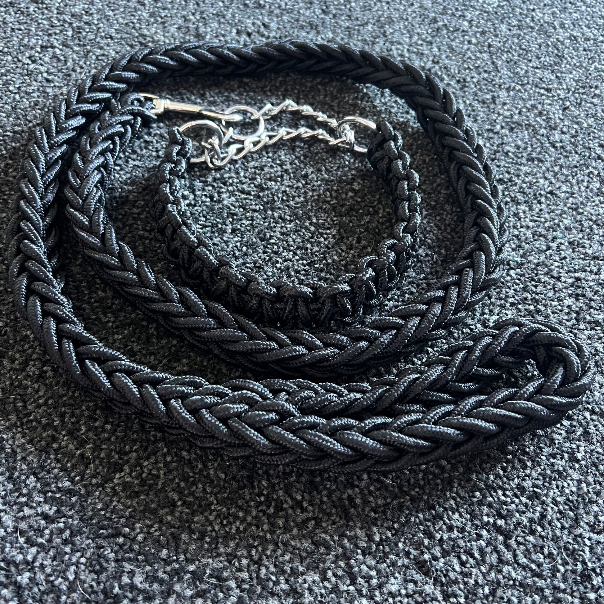 Black braided dog collar with a silver buckle on a textured gray surface