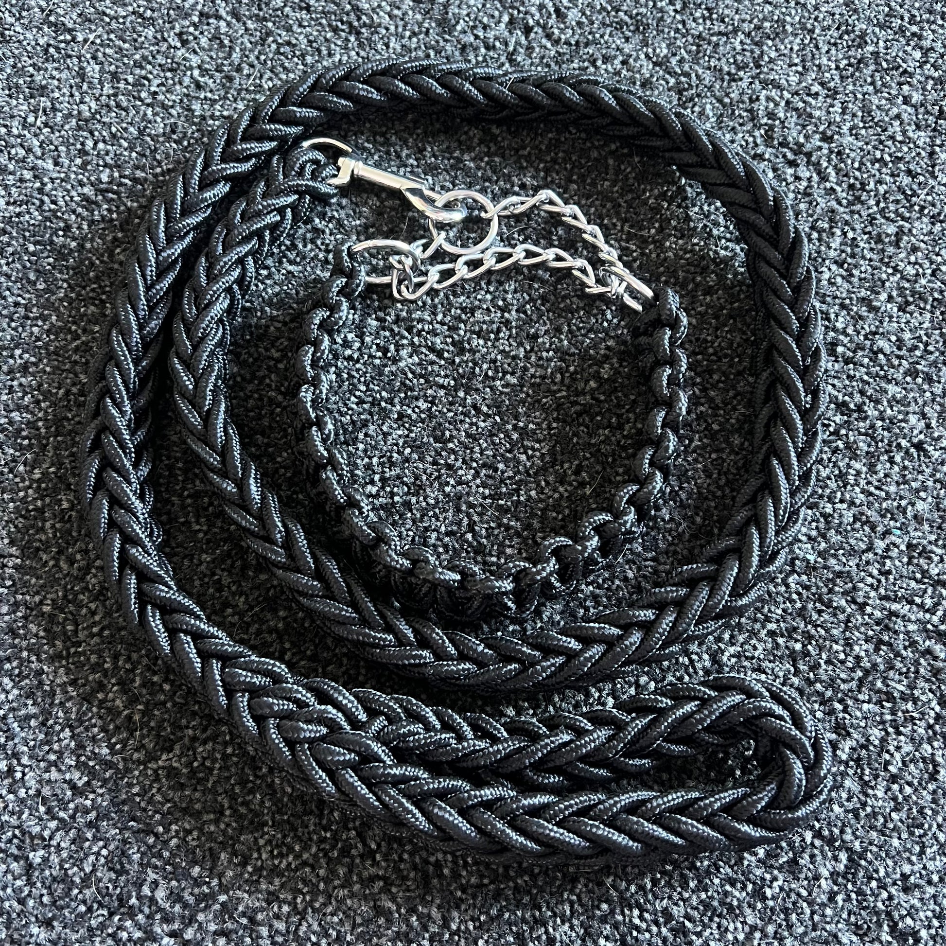 Black braided dog collar with a silver buckle on a textured gray surface